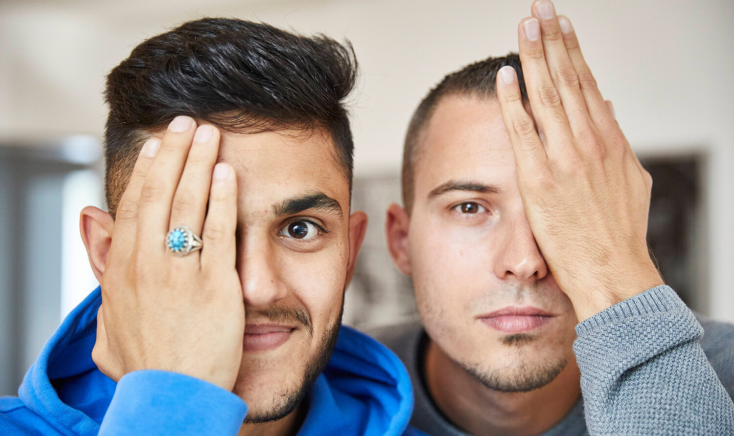 Foto: Zwei junge Männer, die sich jeweils ein Auge mit der Hand zuhalten