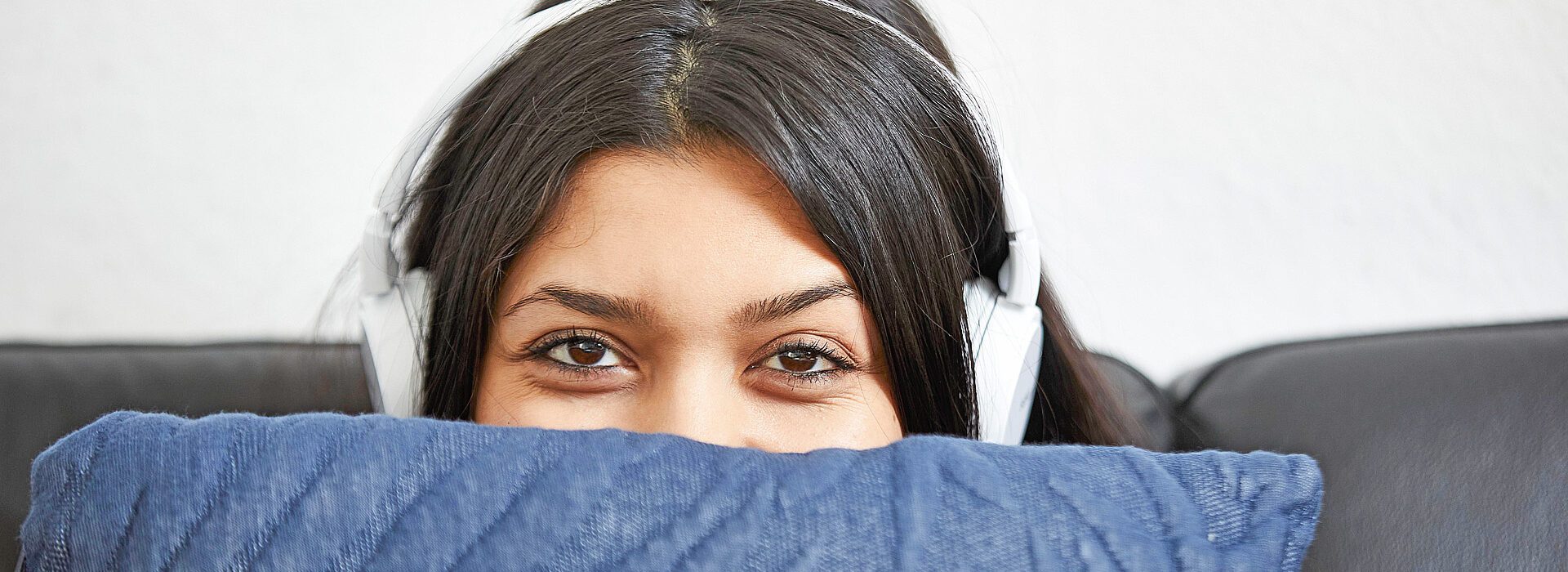 Foto: Junge Frau mit Kopfhörern hält ein Kissen - sozialpädagogisch betreutes Wohnen